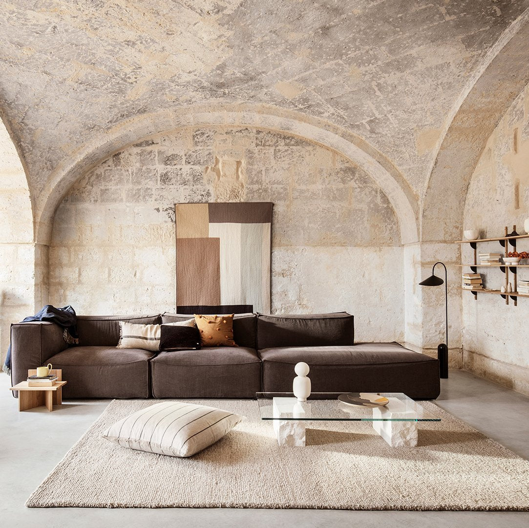 Brown sectional sofa in a minimalist space, complemented by neutral earth tones and geometric wall art. Soft textures throughout.