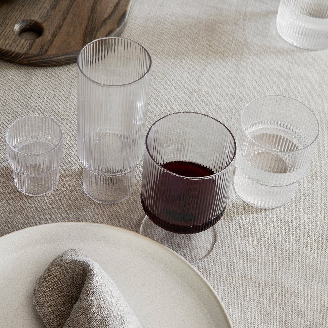 Set of four ribbed glass tumblers in clear, smoky gray, and rich burgundy, showcasing elegant, textured patterns.