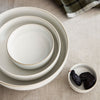 Three elegant cream bowls with subtle gold rims, arranged on a textured linen surface. Small dish with dark fruits.