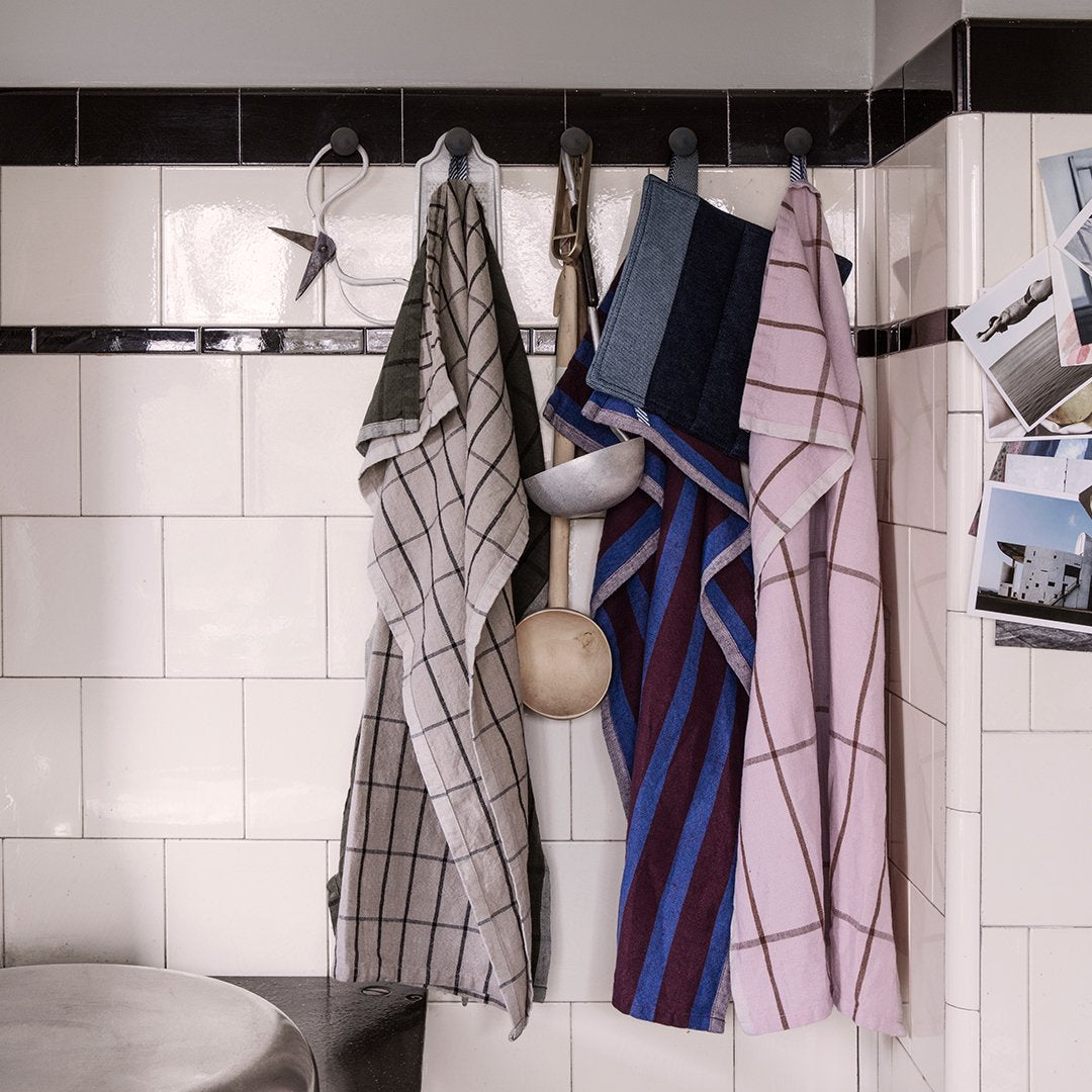 "Set of checked kitchen towels in gray, blue, maroon, and pink hanging on hooks against a tiled wall."