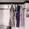 "Set of checked kitchen towels in gray, blue, maroon, and pink hanging on hooks against a tiled wall."