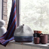 Gray and blue striped knitted hat with maroon and blue patterned textiles and assorted coffee mugs.