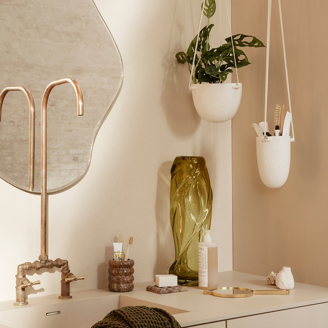 "Elegant green glass vase, white hanging planter, and neutral tones create a warm, modern aesthetic."