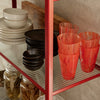 Colorful glassware in vibrant red patterns, with contrasting black and neutral dishware on a metal shelf.