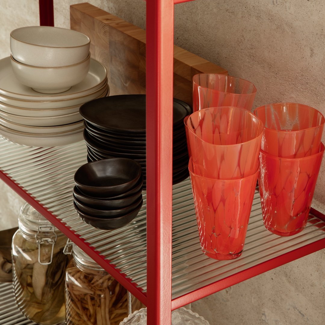 "Colorful glassware in vibrant orange-red, paired with black and neutral dishware on metal shelving."