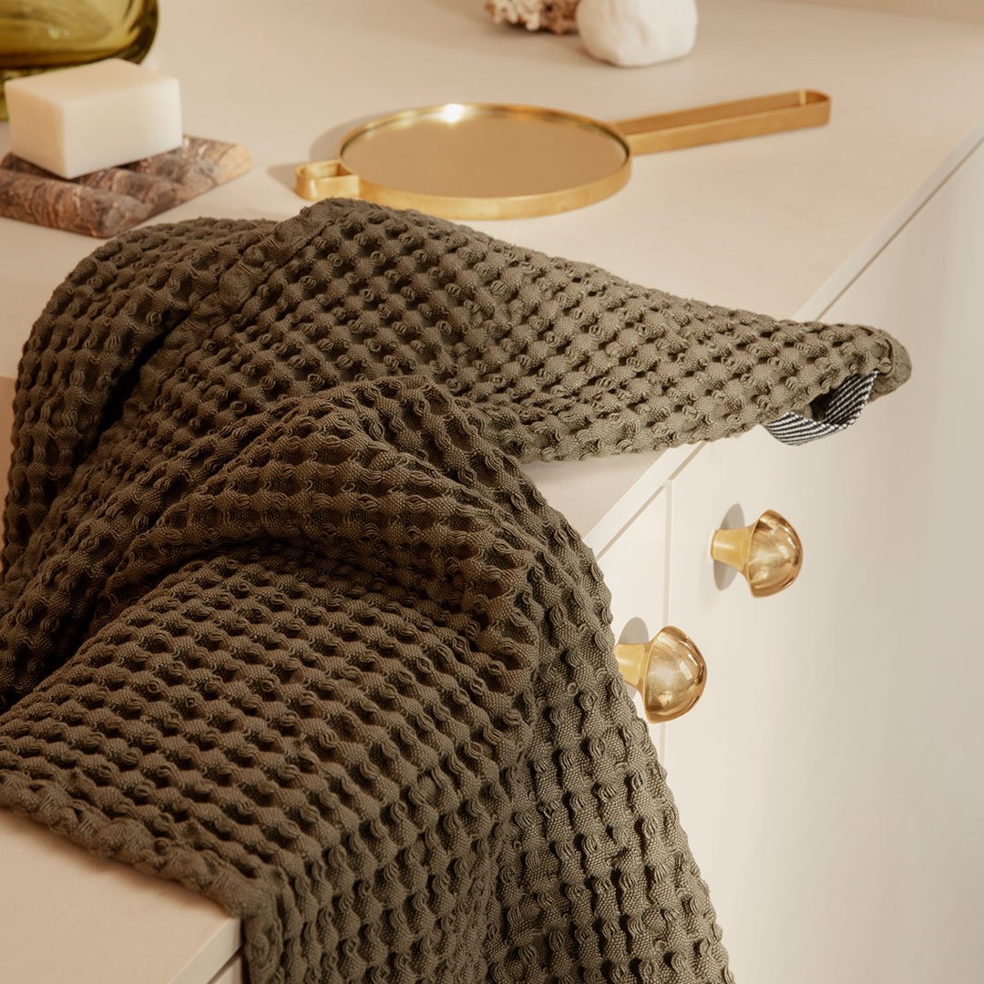 Olive green textured waffle blanket draped elegantly on a beige surface, showcasing a cozy, modern aesthetic.