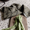 Olive green dish towel with a black grid pattern, resting on a wooden board with green beans.