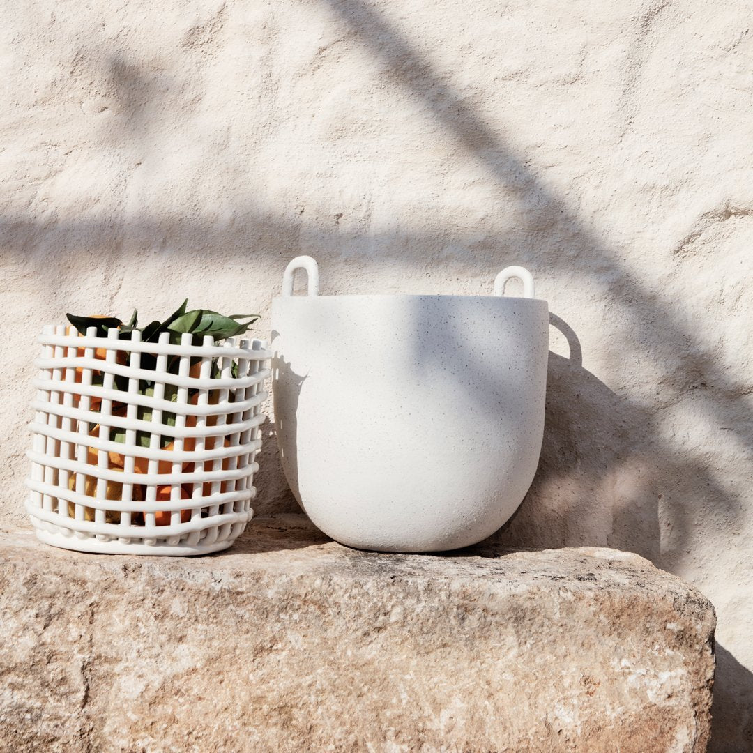 "White rounded planter and grid-patterned basket against a textured stone background, featuring earthy tones."