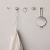"White fabric bag hanging from gold and crystal accents on a light gray wall, showcasing elegant simplicity."