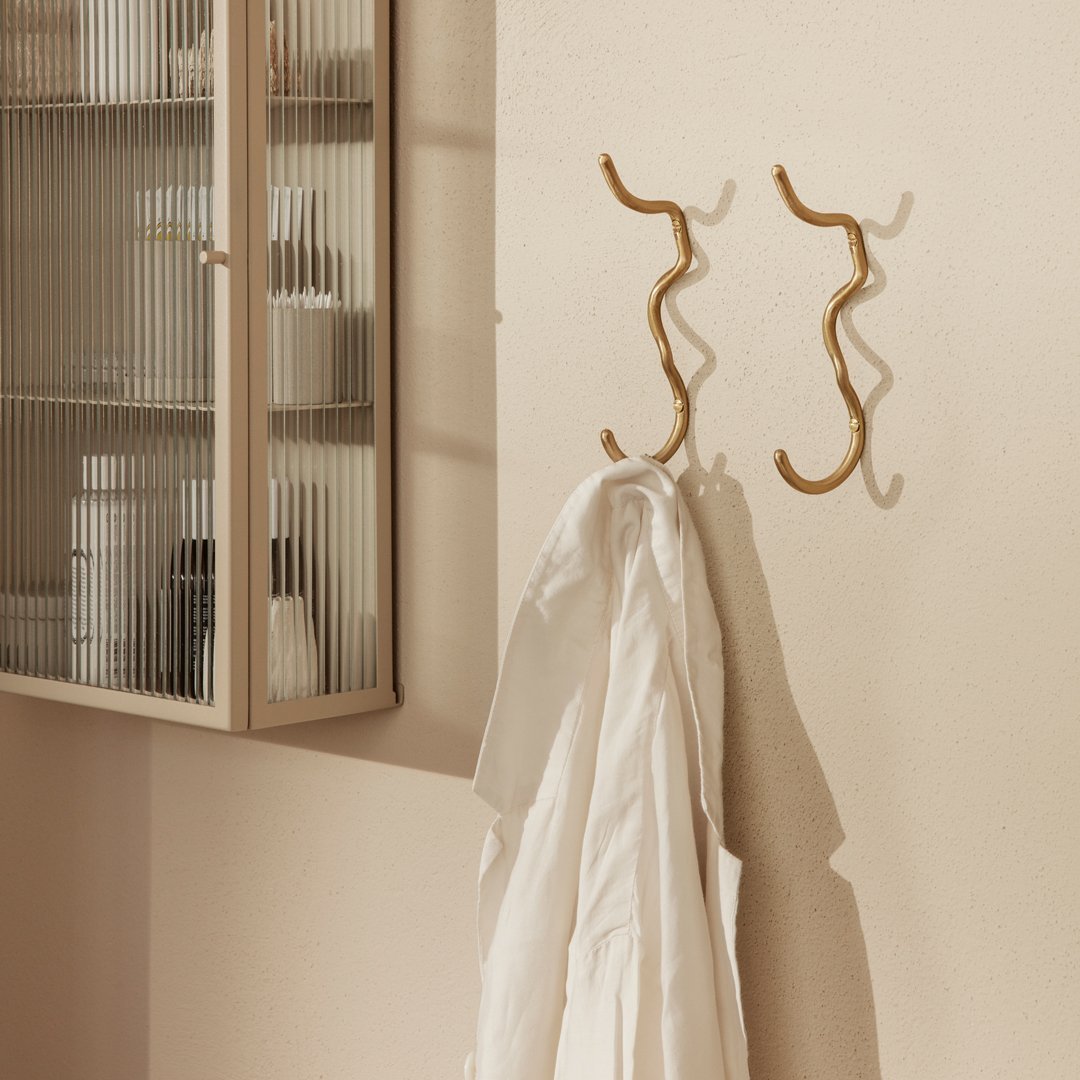 Gold wavy hooks on a soft beige wall, showcasing a sleek, modern design with clean lines.