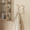Gold wavy hooks on a soft beige wall, showcasing a sleek, modern design with clean lines.
