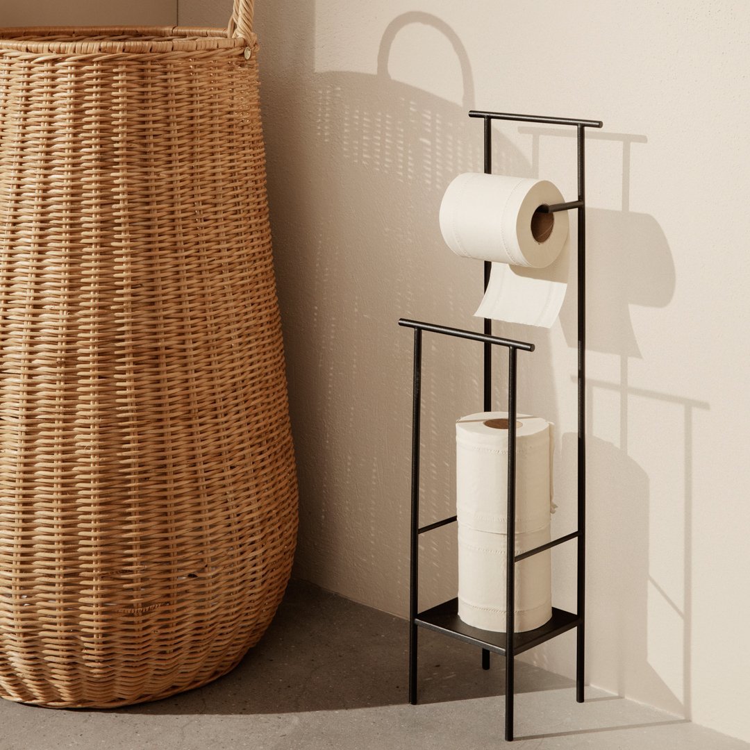 Black metal toilet paper holder with white rolls and a warm beige decorative basket, featuring natural woven patterns.