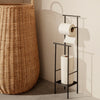 Black metal toilet paper holder with white rolls and a warm beige decorative basket, featuring natural woven patterns.