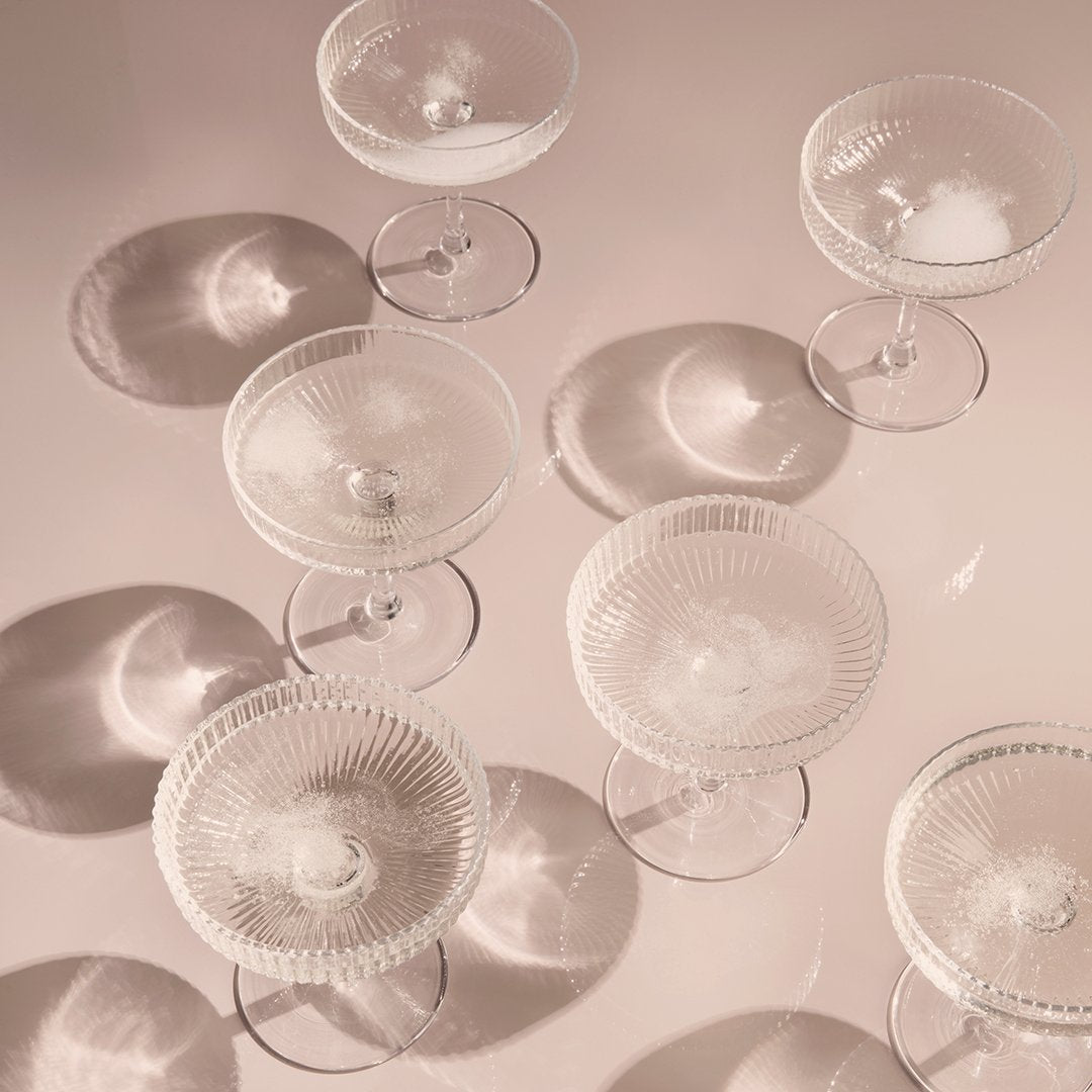 Elegant clear glass dessert bowls with intricate patterns and soft shadows on a pastel surface.