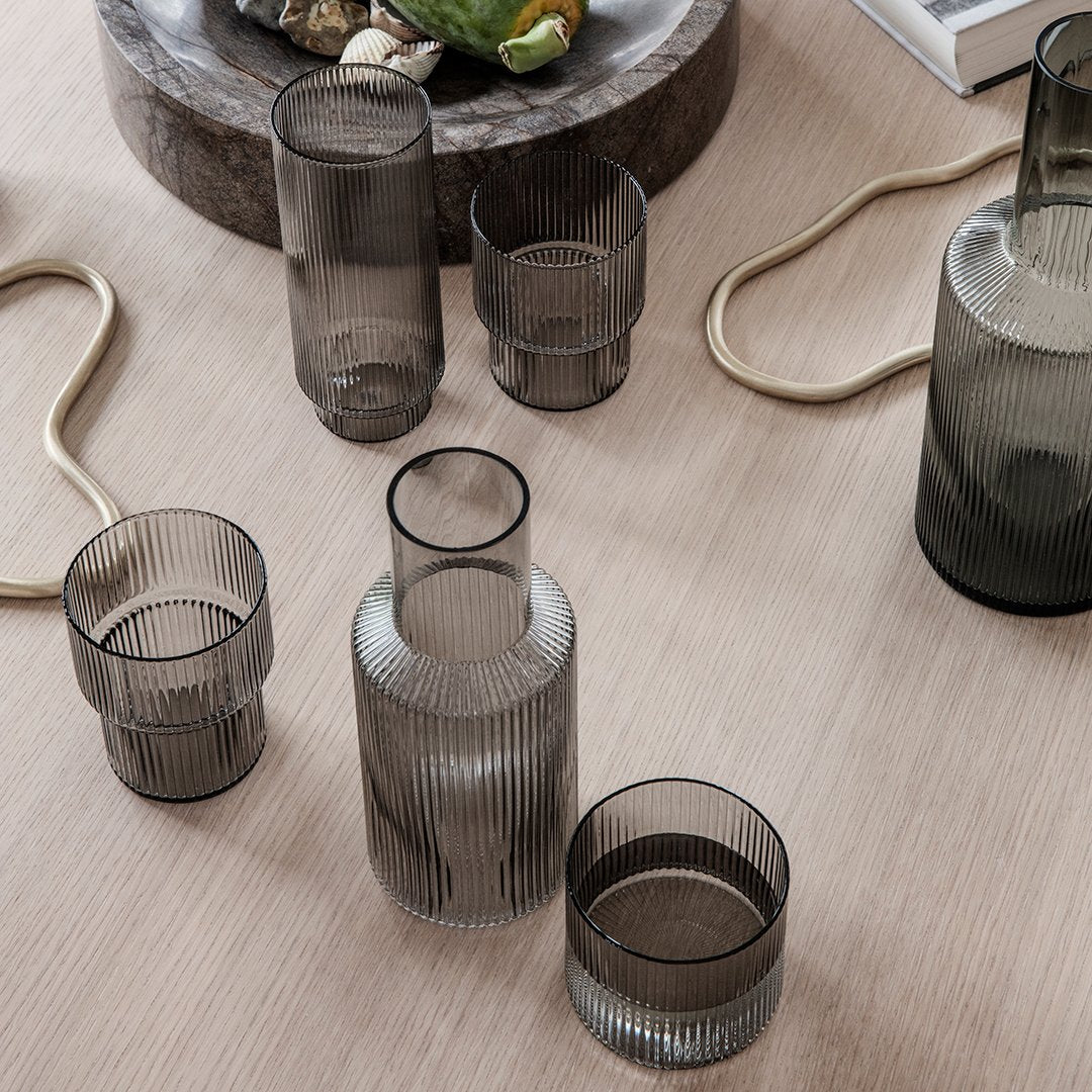 "Smoky gray glass vessels with vertical ribbed patterns on a light wooden surface."