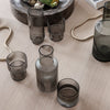 Set of sophisticated smoke-colored glass vases and cups with elegant ribbed patterns on a wooden surface.