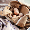 Brown linen cloth with navy stripes, draped over a bowl of eggs, on a rustic wooden surface.