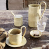 "Set of rustic yellow ceramic drinkware with a speckled texture, featuring a mug, pitcher, sugar jar, and dish."