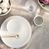 Neutral-toned dining set featuring smooth ceramic plates, a glass, and minimalist designs on a textured linen tablecloth.