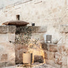 Neutral tones with textured patterns on a decorative pillow and minimalist planters set against a rustic stone backdrop.