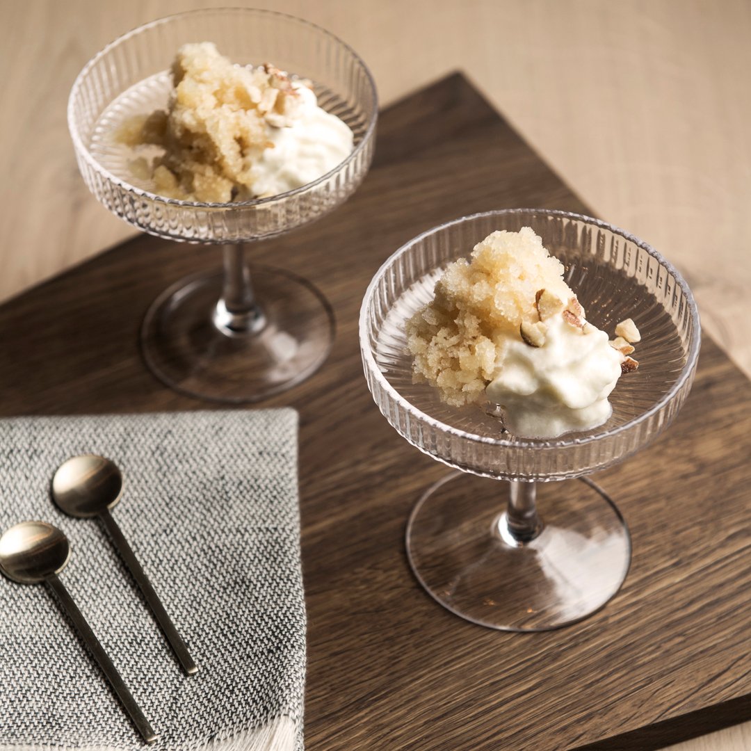 Two clear glass dessert cups with textured patterns, filled with creamy desserts, set on a dark wood surface.