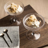 Two clear glass dessert cups with textured patterns, filled with creamy desserts, set on a dark wood surface.