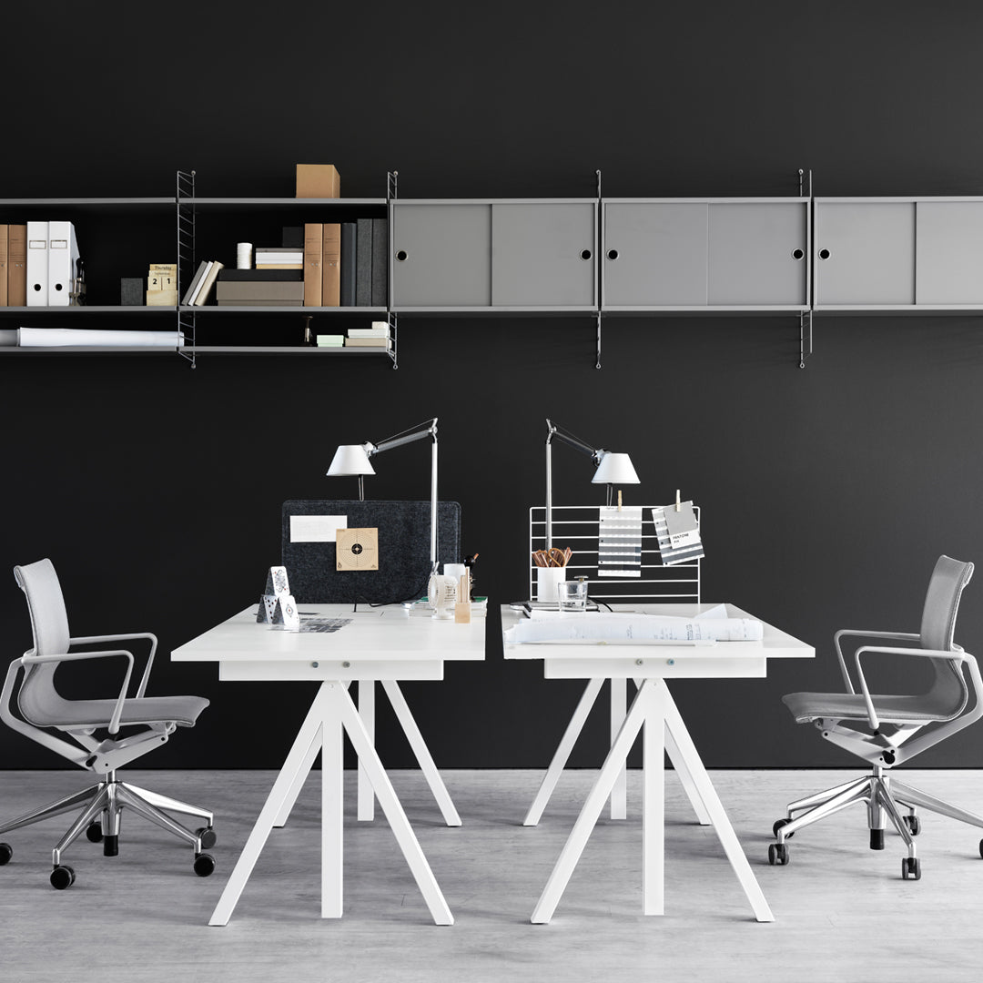Modern white desks with geometric legs, sleek gray shelving, and a bold black wall create a stylish office workspace.
