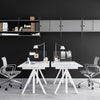Modern white desks with geometric legs, sleek gray shelving, and a bold black wall create a stylish office workspace.