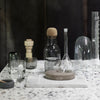 Clear glassware with cork and stone accents on a speckled white surface. Elegant, modern design aesthetic.