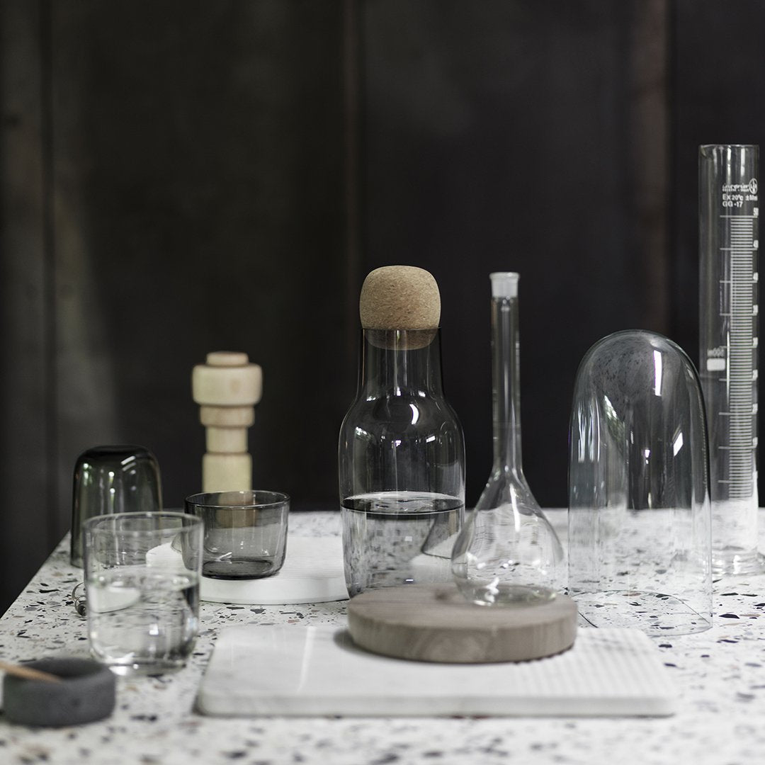 Clear glass and cork containers on a terrazzo tabletop, featuring textured patterns and sleek, modern designs.