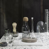 Clear glass and cork containers on a terrazzo tabletop, featuring textured patterns and sleek, modern designs.