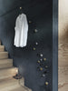 White shirt hanging on a dark textured wall, featuring varied metal hooks in gold, brass, and natural stone colors.