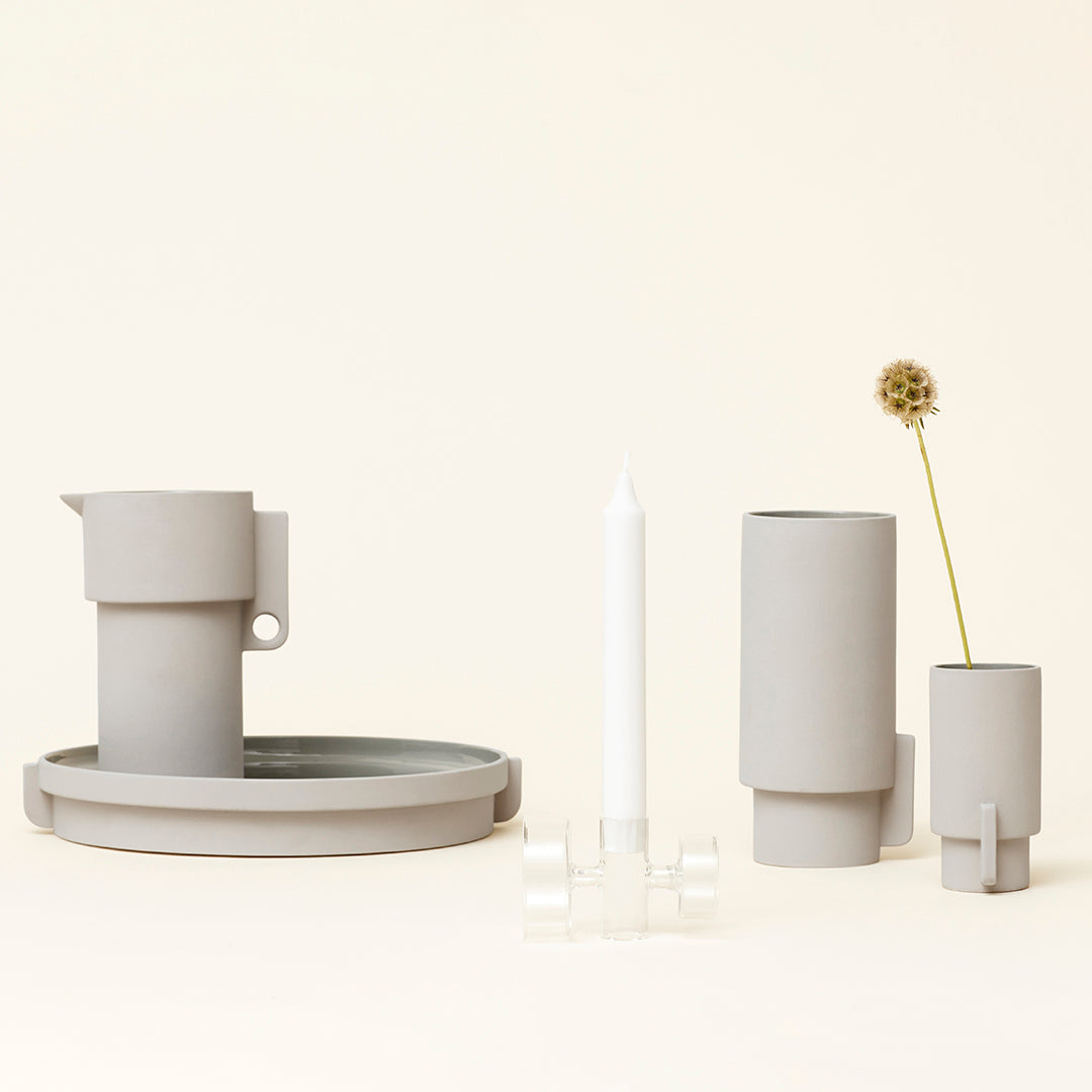 Soft gray ceramic set with minimalist shapes and a smooth matte finish, featuring a candle holder and vase.