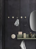 "Dark textured wall with brass hooks, green shelf, and a round mirror for a modern, minimalist aesthetic."