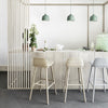 Light wood cabinetry, pale gray and beige bar stools, and green pendant lights create a fresh, modern aesthetic.