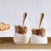 Two clear glass cups filled with layered yogurt and granola, featuring a creamy white and brown color scheme.
