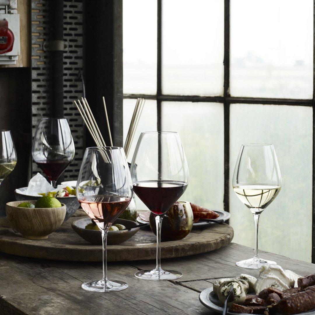 Elegant glassware featuring red, white, and rosé wines beside a rustic wooden table with green and earthy tones.