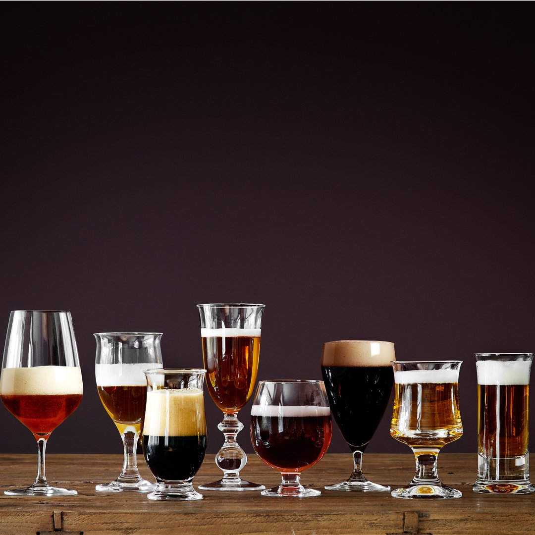 Assorted glasses filled with various shades of amber, brown, and golden beers against a dark background.