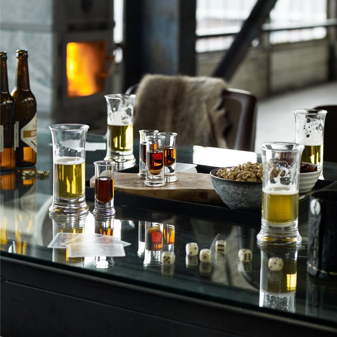 Assorted glasses with golden beers, dark shots, and pops of red, arranged on a rustic table with a reflective surface.
