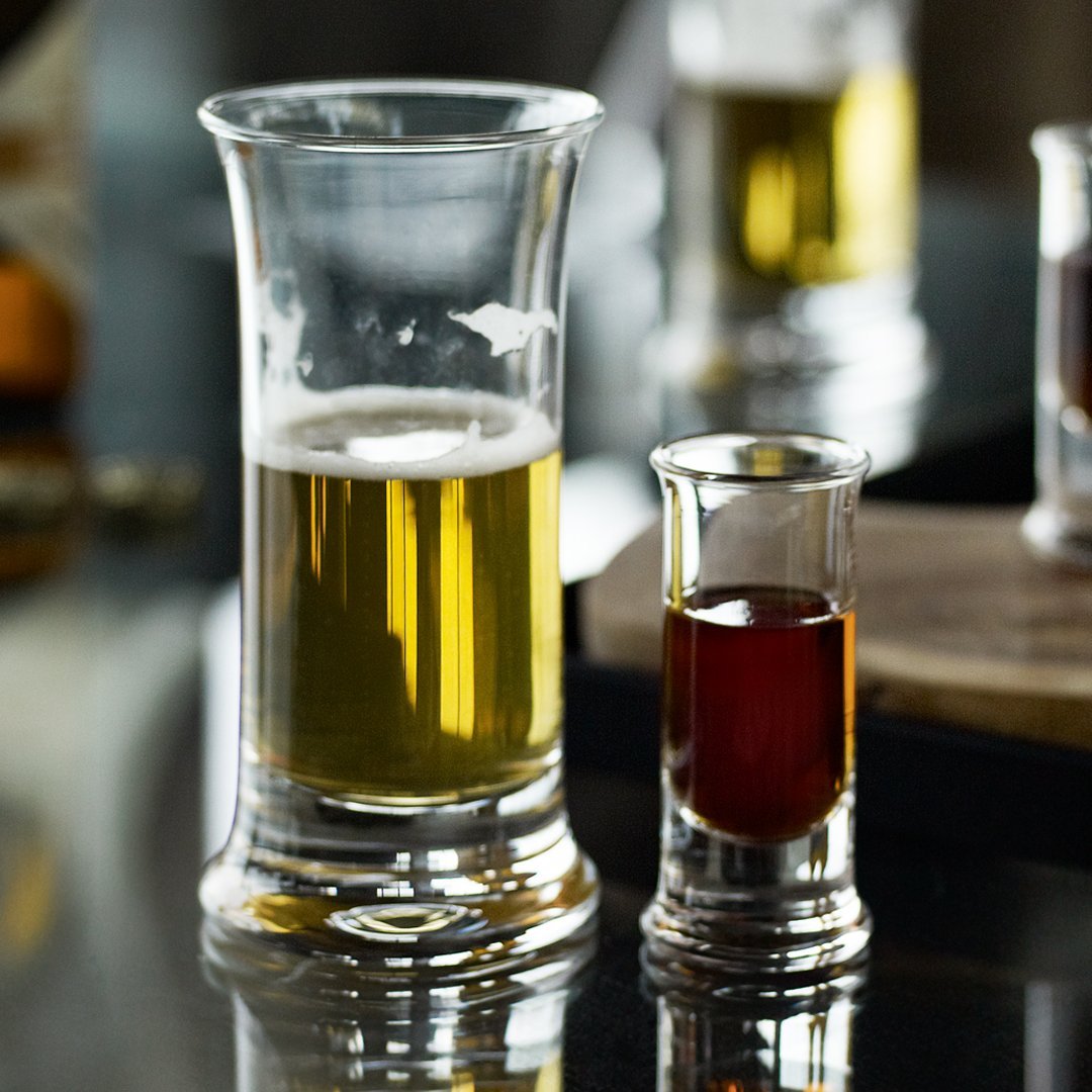 "Clear glass shot and beer glasses showcasing rich amber and golden hues, set against a sleek black surface."