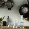 Clear glassware set on a wooden table, featuring varying heights and simple patterns, against a muted green backdrop.