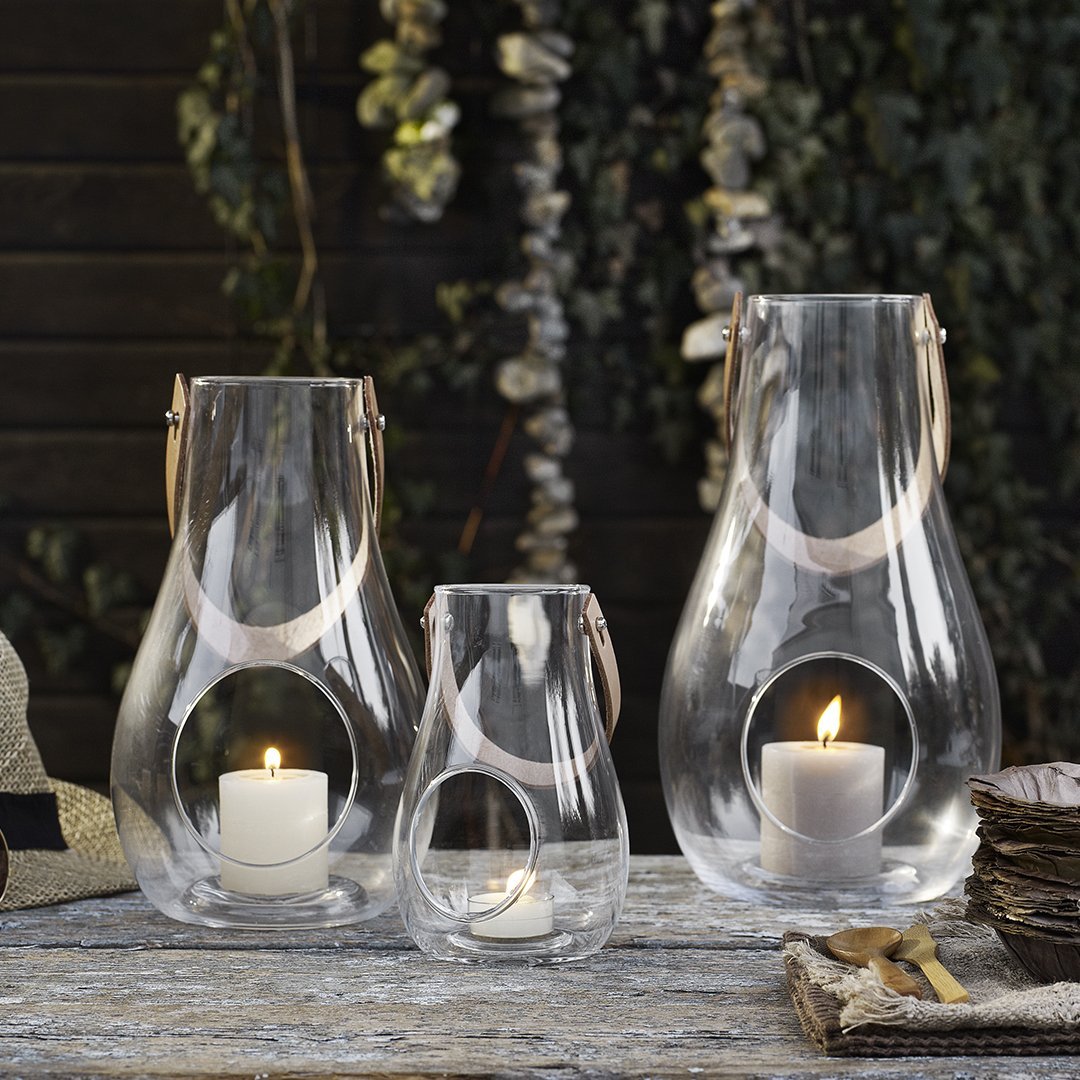 Set of three clear glass lanterns with light beige straps, featuring rounded shapes and soft candlelight glow.