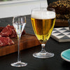 Clear glassware displaying golden beer and sparkling liquid, set against a contrasting black table and patterned coaster.