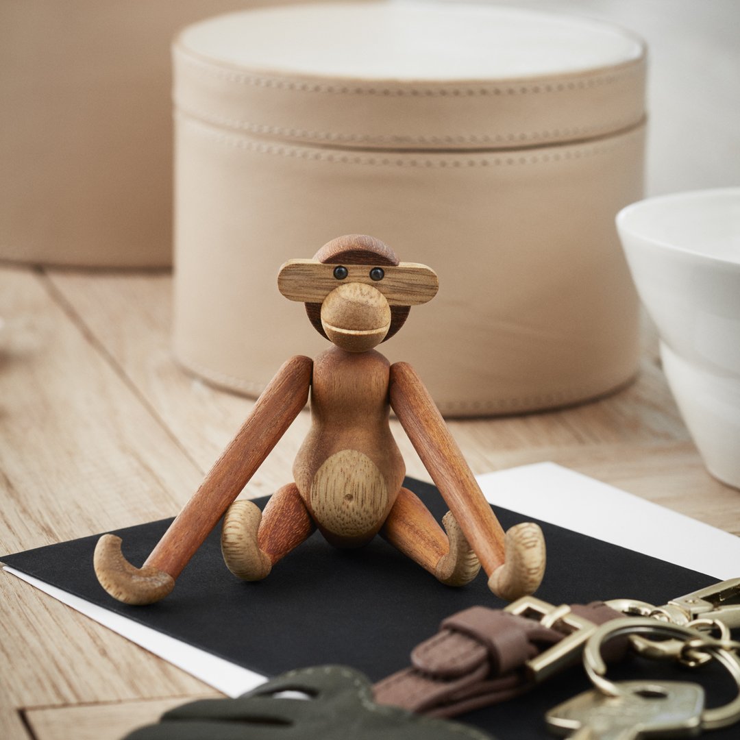 Wooden monkey figurine in natural hues with a smooth finish, set against a minimalist background of black and beige.