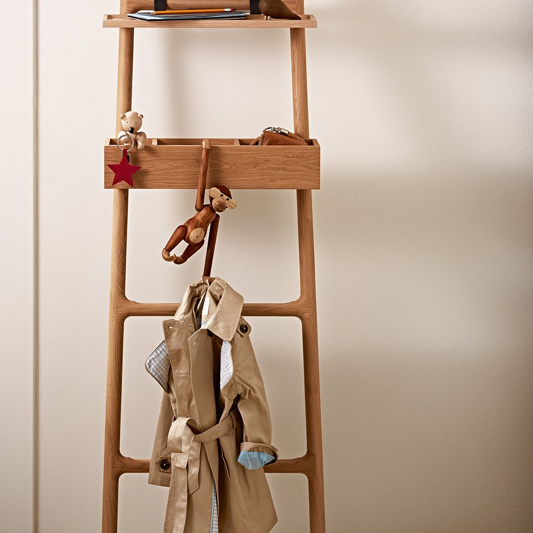 Wooden ladder shelf in light brown with a beige coat, wooden toys, and red accents. Simple, functional design elements.