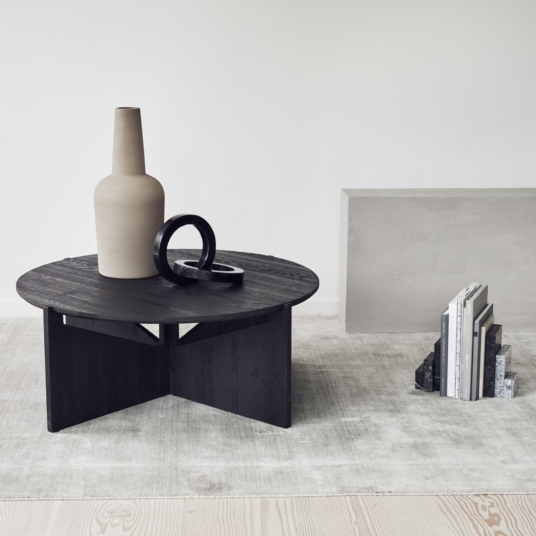 Round black coffee table with a textured wood finish, paired with a neutral beige vase and contrasting black accents.