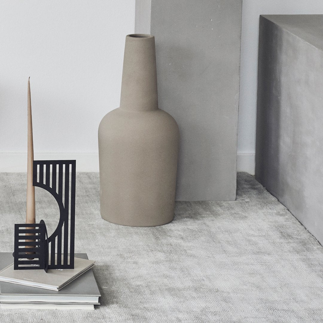 Gray ceramic vase with a modern, minimalist design on a textured light gray surface, complemented by black accents.