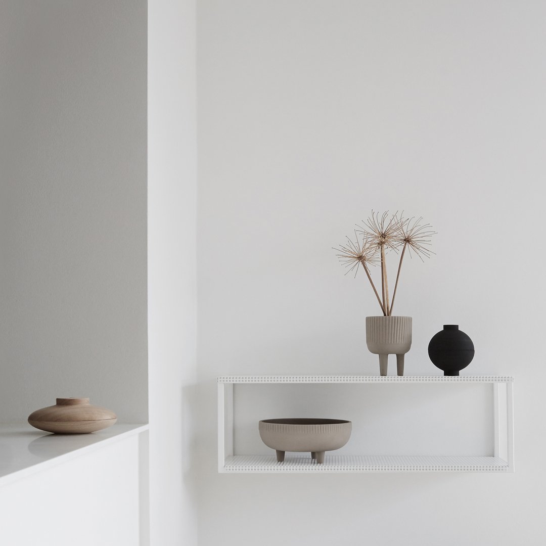 Neutral tones with soft beige and black accents; minimalist decor on a white shelf against a light background.