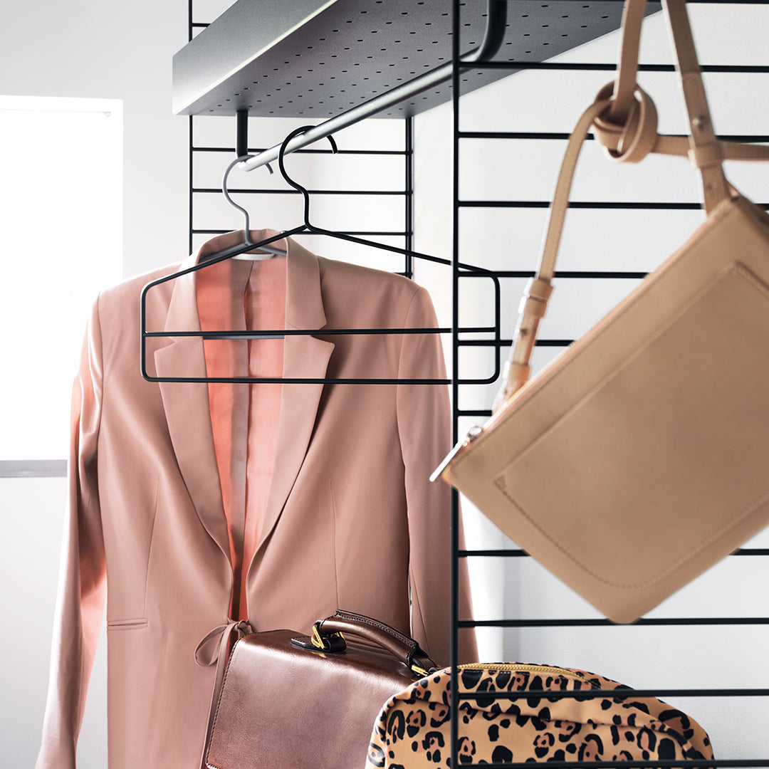 Blush pink suit jacket, beige handbag, and leopard print bag displayed on a sleek black hanger against a modern backdrop.