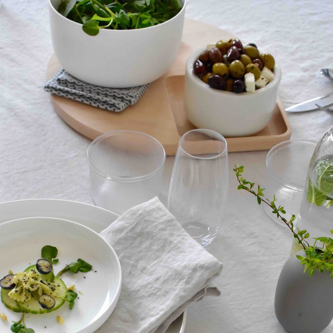Elegant white dinnerware with a neutral cloth, accented by green salad and wooden serving tray, showcasing a modern dining setup.